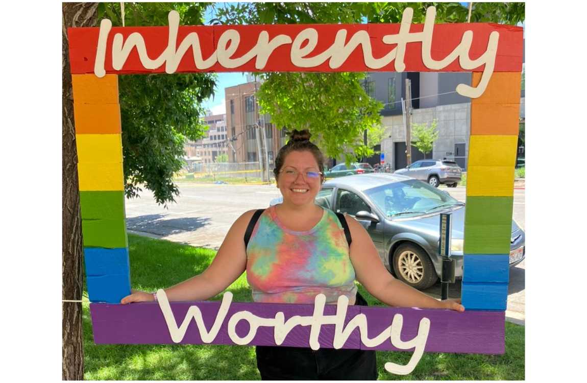 Grace, a Queer Fat Woman, stands in a rainbow frame stating "Inherently Worthy."